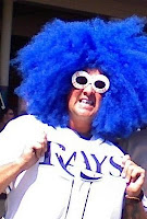 Person with blue wig and sunglasses cheering.