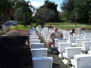 People sitting on toilets outdoors reading newspapers.