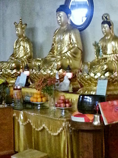 Golden Buddha statues with offerings on altar.