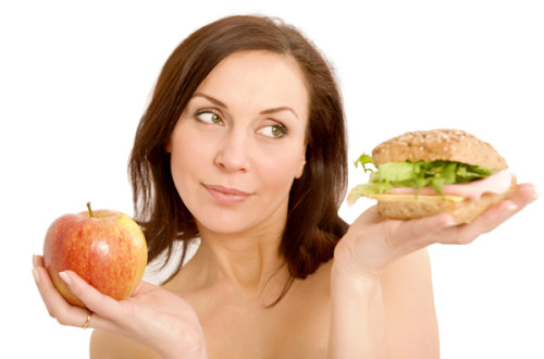 A woman holding an apple and a hamburger.