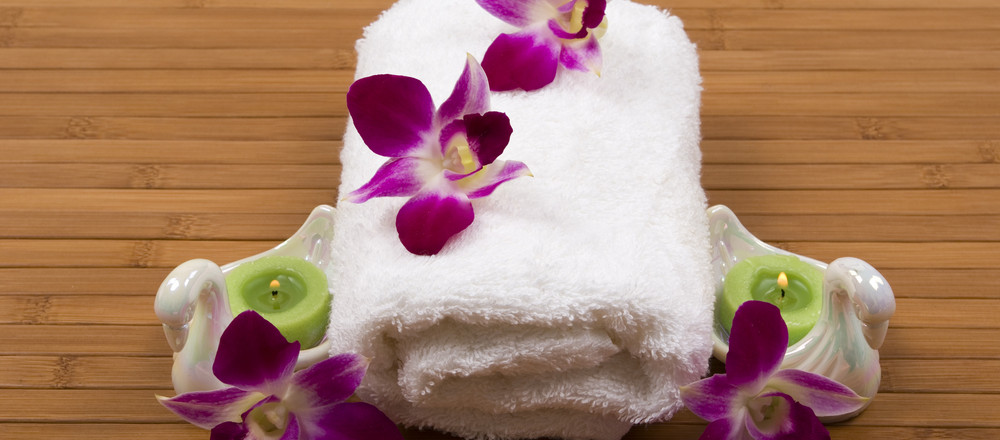 Stack of white towels decorated with purple orchids on bamboo mat.