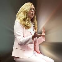 Debbie Lane, certified hypnotherapist, seated in a light pink suit, speaking with expressive hand gestures in a softly illuminated setting.